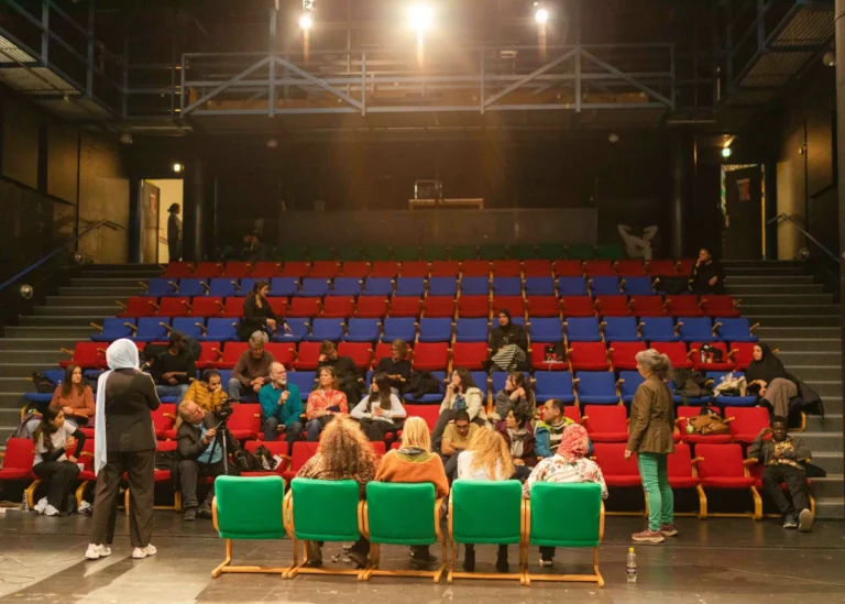 På scenen sidder fem personer på stole foran et lille publikum